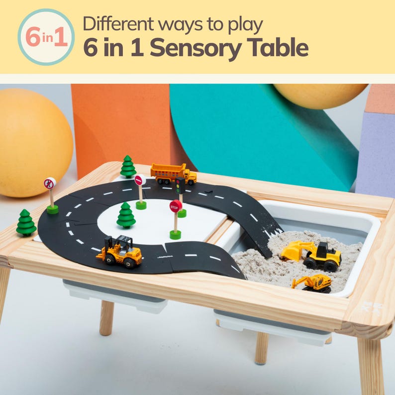 May include: A wooden sensory table with a black road track, toy construction vehicles, and a sand pit. The table has a white removable tray and a 6 in 1 label.