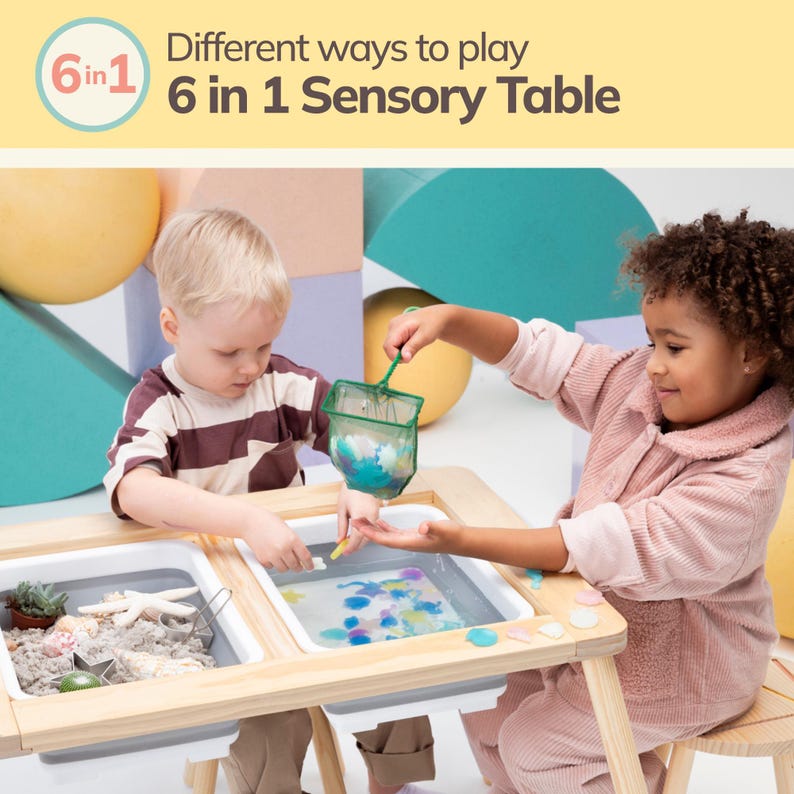 May include: Two children play with a 6 in 1 Sensory Table. The table has four compartments, two with water and two with sand. The children are using a net to scoop up objects from the water. The table is made of wood and has a light wood finish.