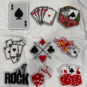 May include: Nine embroidered iron-on patches featuring playing cards, dice, and the word "ROCK" with a guitar. The patches are white, red, black, and green.