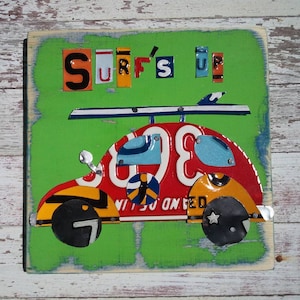 May include: A green wooden sign with a red, yellow, and blue Volkswagen Beetle made from recycled license plates. The sign says "Surf's Up" in colorful letters.