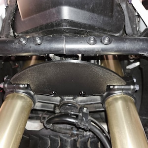 Puede incluir: Primer plano de un guardabarros de motocicleta negro con una superficie texturizada. El guardabarros está sujeto a las horquillas delanteras de una motocicleta.