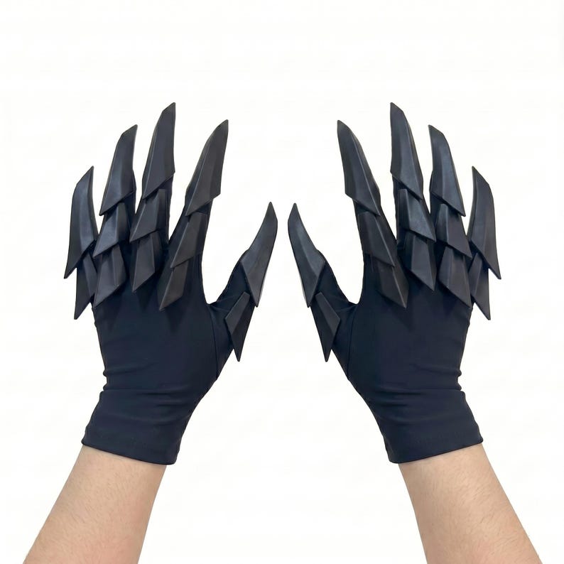 Puede incluir: Un par de guantes negros con estructuras articuladas en capas, similares a garras, que se extienden desde los dedos y el dorso de la mano. Los guantes est&aacute;n hechos de una tela oscura y lisa con accesorios r&iacute;gidos, puntiagudos y escamosos.