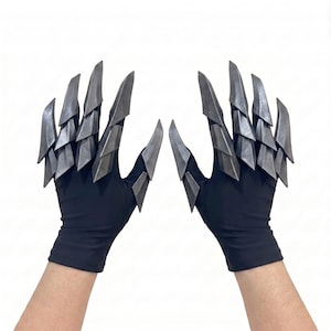 Puede incluir: Un par de guantes negros con extensiones met&aacute;licas plateadas articuladas en forma de garra unidas a los dedos y pulgares. Las placas r&iacute;gidas y superpuestas crean una apariencia afilada y segmentada en el dorso de la mano y cada dedo.