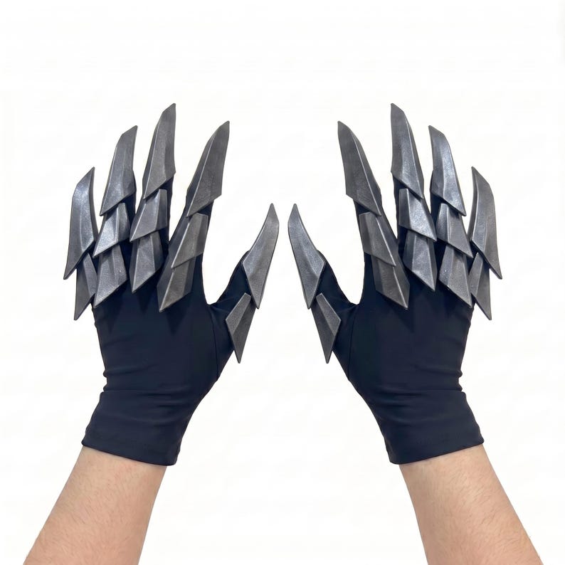 Puede incluir: Un par de guantes negros con extensiones met&aacute;licas plateadas articuladas en forma de garra unidas a los dedos y pulgares. Las placas r&iacute;gidas y superpuestas crean una apariencia afilada y segmentada en el dorso de la mano y cada dedo.