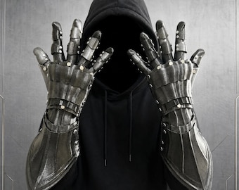 May include: A pair of articulated dark metallic gauntlets featuring segmented finger plates and a long forearm guard. The armor pieces are connected with small silver rivets, creating a flexible structure that covers the hands and wrists.