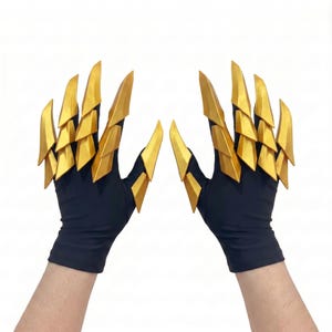 Puede incluir: Un par de guantes negros con accesorios en forma de garras doradas articuladas en cada dedo. Los segmentos dorados r&iacute;gidos, superpuestos y triangulares se extienden desde los nudillos hasta las puntas de los dedos, creando un aspecto afilado.