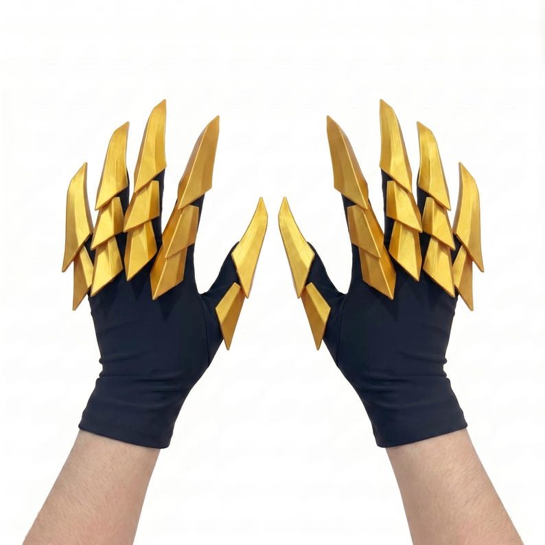 Puede incluir: Un par de guantes negros con accesorios en forma de garras doradas articuladas en cada dedo. Los segmentos dorados r&iacute;gidos, superpuestos y triangulares se extienden desde los nudillos hasta las puntas de los dedos, creando un aspecto afilado.