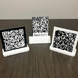 May include: Three white plastic stands with black and white QR codes printed on them. The middle stand has the text "Need Wi-Fi?" printed on it.