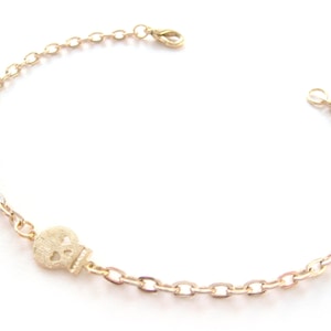 May include: A gold chain bracelet with a small gold skull charm. The chain is made of oval links.