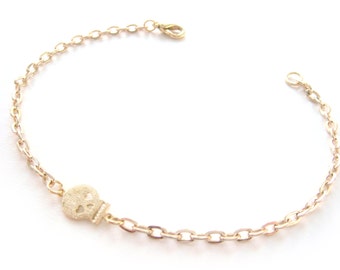 May include: A gold chain bracelet with a small gold skull charm. The chain is made of oval links.