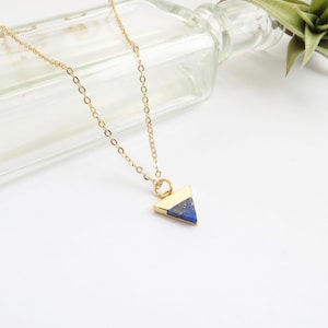 May include: A gold chain necklace with a triangular pendant made of lapis lazuli stone. The pendant is a dark blue color with gold accents.