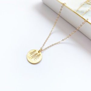 May include: A gold necklace with a round pendant featuring a hammered texture and a design of three trees.