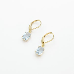 May include: A pair of gold earrings with light blue gemstone drops.