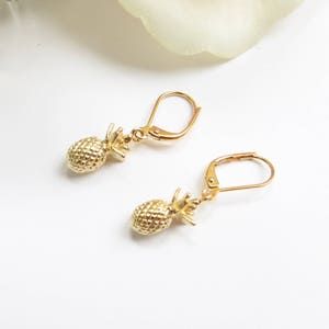 Op de afbeelding: Een paar gouden ananas oorbellen met oorhaakjes. De oorbellen zijn gemaakt van metaal en hebben een getextureerd ananas ontwerp.