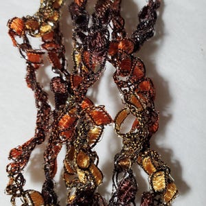 May include: A close-up of a crocheted trim with brown, orange, and gold threads. The trim has a delicate, lacy pattern.