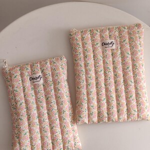 Può includere: Due pochette in tessuto trapuntato con un motivo floreale rosa, giallo e verde. Le pochette hanno un design cucito verticale e una chiusura a cerniera. Ogni pochette ha un'etichetta con la scritta "ChiaraGi Handmade".