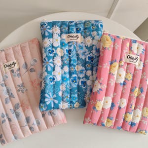 Può includere: Tre pochette in tessuto trapuntato rosa, blu e con motivi floreali. La pochette rosa presenta un disegno di rose, quella blu un motivo a margherite e la terza un motivo floreale. Ogni pochette ha un'etichetta con la scritta "Chiaragi Handmade".