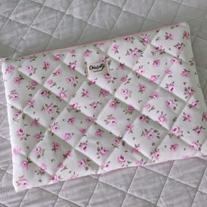 Può includere: Una custodia trapuntata per laptop con motivo floreale, cerniera rosa e tiretto a nappa bianco. La custodia presenta un motivo ripetuto di rose rosa su sfondo verde chiaro. L'etichetta recita "Chiarati handmade".