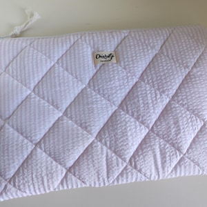 Puede incluir: Bolso de mano rectangular acolchado con un patrón de rayas rosas y blancas. El bolso presenta un patrón de diamantes diagonales y un tirador de cremallera blanco. Una pequeña etiqueta dice "Chiaralgi handmade".