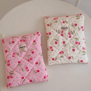 May include: Two rectangular quilted pouches with zipper closures. One pouch is light pink and the other is off-white, both featuring a pattern of red cherries with green leaves and small black dots. Each pouch has a label reading ChiaraGi Handmade.