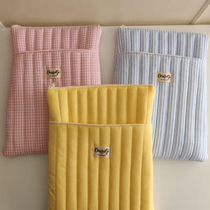 Puede incluir: Tres fundas de tela acolchada en rosa a cuadros, amarillo con lunares blancos y azul y blanco a rayas. Cada funda tiene cierre de cremallera y una pequeña etiqueta que dice "Chiaralgi Handmade".