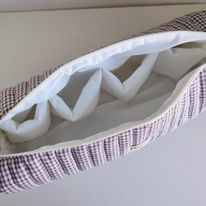 May include: Open, zippered case with a brown and white checkered pattern. The interior is white with several padded dividers. The case is designed to hold and protect items.