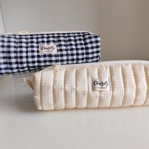 Könnte beinhalten: Zwei gesteppte Federmäppchen. Eines ist schwarz-weiß kariert, das andere hellgelb kariert. Beide haben einen Reißverschluss und ein kleines Stoffetikett mit der Aufschrift "ChiaraGi Handmade".