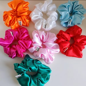 Può includere: Una collezione di scrunchies in raso in vari colori, tra cui arancione, bianco, azzurro, rosa acceso, rosa chiaro, rosso e verde acqua. Ogni scrunchie ha un'etichetta con testo. Questi accessori per capelli sono perfetti.