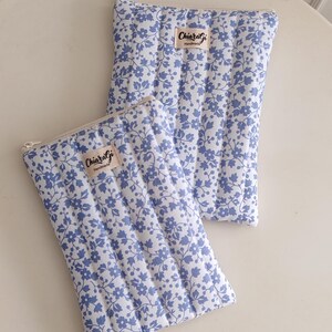 Può includere: Due pochette trapuntate con un motivo floreale blu su sfondo bianco. Ogni pochette ha una chiusura a cerniera e una piccola etichetta con la scritta "ChiaraGi Handmade". Le pochette sono su una superficie bianca.