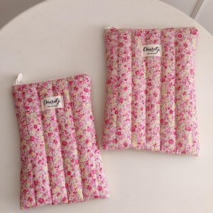 Può includere: Due pochette in tessuto trapuntato con un motivo floreale rosa, giallo e bianco. Ogni pochette ha una chiusura a cerniera e una piccola etichetta che dice "Chiaralgi Handmade". Le pochette sono rettangolari e sembrano imbottite.