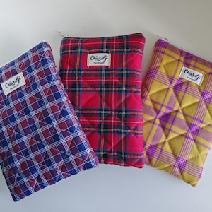 Könnte beinhalten: Drei gesteppte Stoffbeutel mit Reißverschlüssen. Die Beutel weisen Karomuster in Rot, Blau und Gelb mit lila Akzenten auf. Jeder Beutel hat ein weißes Etikett mit dem Text "ChiaraGi Handmade".