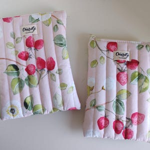 Peut inclure: Deux pochettes matelassées roses avec un imprimé fraise et floral. Le motif présente des fraises rouges, des feuilles vertes et des fleurs blanches sur un fond rose clair. Chaque pochette a une fermeture éclair et une étiquette "ChiaraGi Handmade".