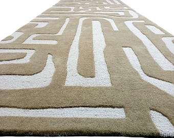 May include: A beige rug with a white geometric pattern. The pattern is made up of lines and curves that create a maze-like design.