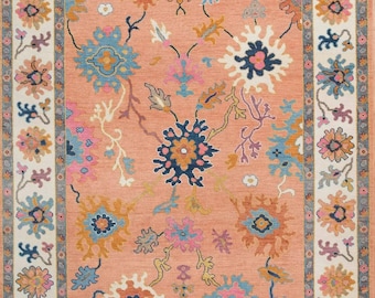 May include: A pink rug with a floral pattern in shades of blue, pink, and orange. The rug has a white border with a floral design.