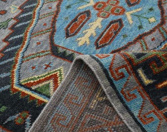 May include: Close-up of a blue, red, and green patterned rug with a gray border. The rug has a geometric design with intricate details.