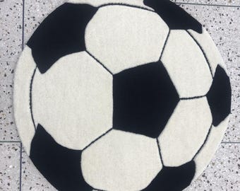 May include: A circular rug featuring a classic black and white soccer ball pattern. The design consists of alternating black pentagons and white hexagons, mimicking the traditional appearance of a soccer ball in a soft, tufted textile format.
