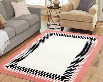May include: A white area rug with a black and white geometric border. The border is on a light pink background.