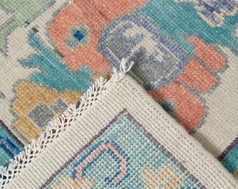May include: A close-up of a white rug with a fringe border. The rug has a colorful geometric pattern in shades of blue, green, pink, and yellow.