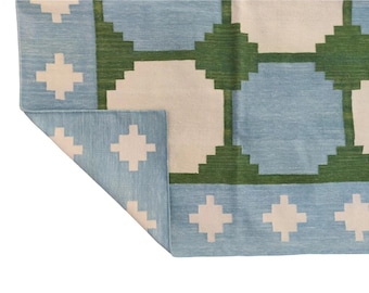 May include: A blue and white rug with a geometric pattern of green squares. The rug has a white border with a cross pattern.
