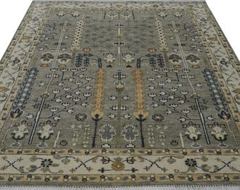 May include: A gray area rug with a detailed floral pattern in shades of beige, brown, and blue. The rug has a fringe border.