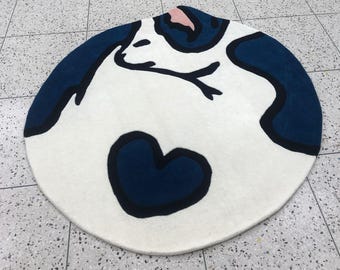 May include: A white round rug with a blue and black abstract design. The design features a heart shape and a stylized animal figure.