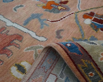 May include: A detailed shot of a peach-colored rug with a floral pattern. The rug features designs in shades of blue, orange, red, and white. A portion of the rug is folded over, revealing the underside with a striped pattern.
