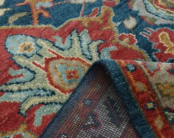 May include: Close-up of a blue, red, and beige patterned rug with a detailed woven design. The rug has a fringed edge and is folded over to show the underside.