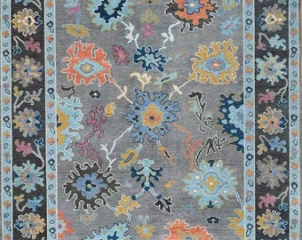 May include: A gray rug with a floral pattern in shades of blue, orange, yellow, and pink. The rug has a border with a repeating pattern of flowers and leaves.