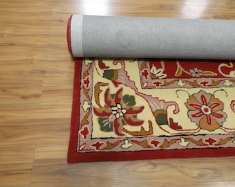 May include: Partially rolled red area rug with a floral pattern. The rug features a cream-colored central field with a repeating floral design in shades of red, green, and pink. The border is a solid red.