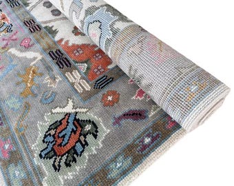 May include: A gray rug with a colorful geometric pattern. The rug has a light blue, pink, and orange design. The rug is rolled up and the back side is visible.
