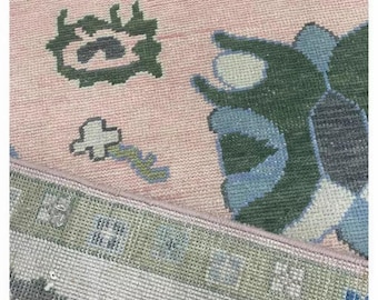 May include: A pink rug with a floral pattern in shades of green, blue, and white. The rug has a fringe border.