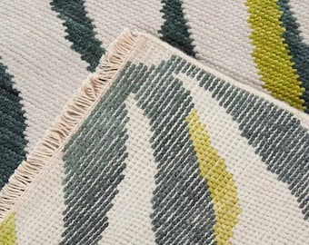 May include: Close-up of a textured rug with a repeating pattern of vertical stripes. The stripes alternate between white, dark teal, and yellow-green. The rug has a fringed edge.