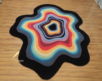 May include: A colorful, abstract area rug with a unique, organic shape. The rug features concentric layers of vibrant colors, including red, orange, yellow, blue, and purple, set against a black border. The rug's design adds a modern touch to any room.