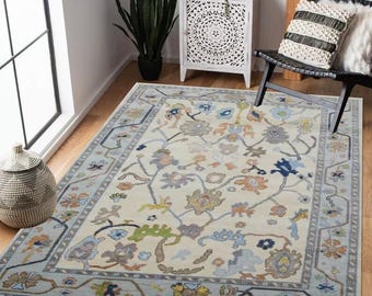 May include: A cream-colored rug with a floral pattern in shades of blue, green, and orange. The rug has a border with a geometric design.